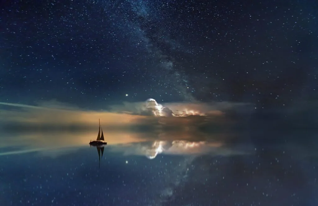 Sailboat with illuminated sail on calm water beneath starry sky and Milky Way