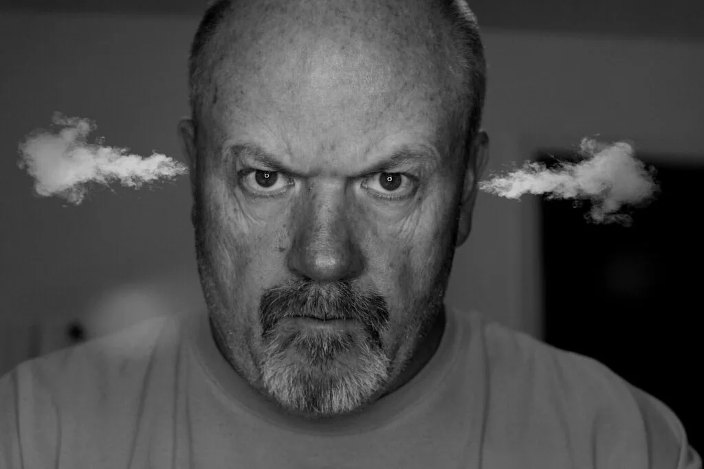 Man with beard and intense expression with steam coming from ears against gray background