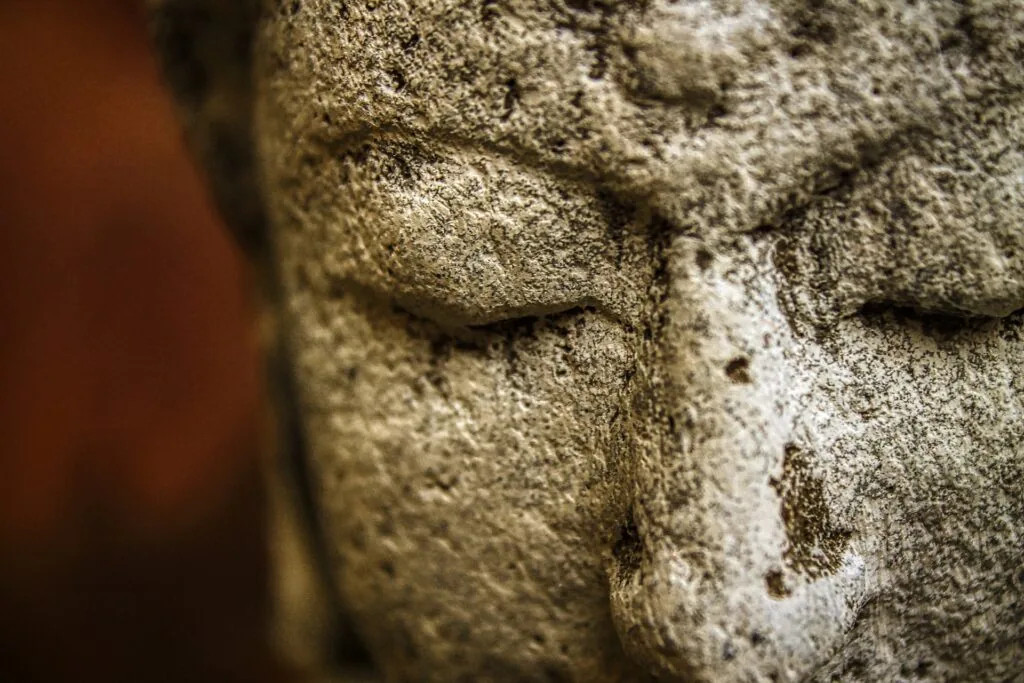 Close-up of weathered stone statue face with closed eyes and textured surface