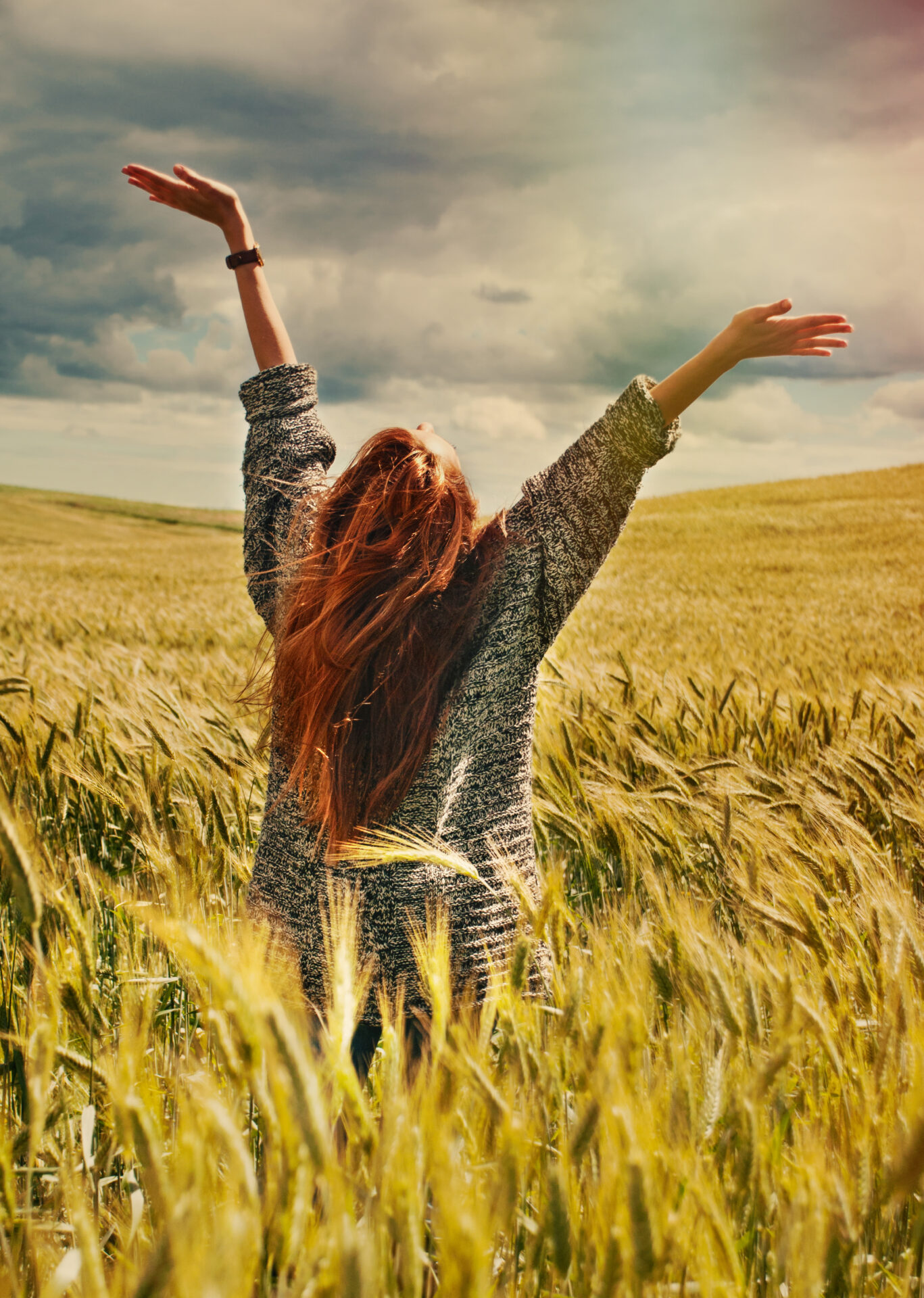 fashion young red hair woman standing back hands up on breathtaking view of dramatic storm sky in the field