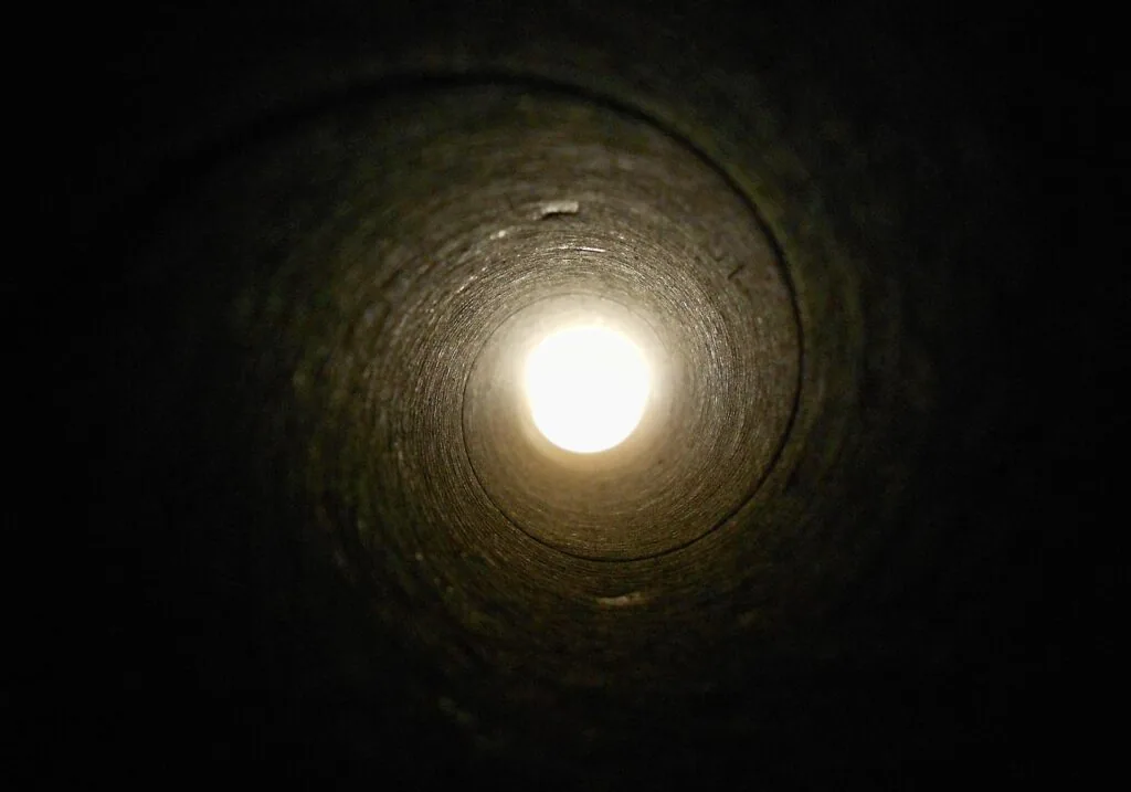 Bright white light visible at the end of a dark spiral tunnel with textured walls