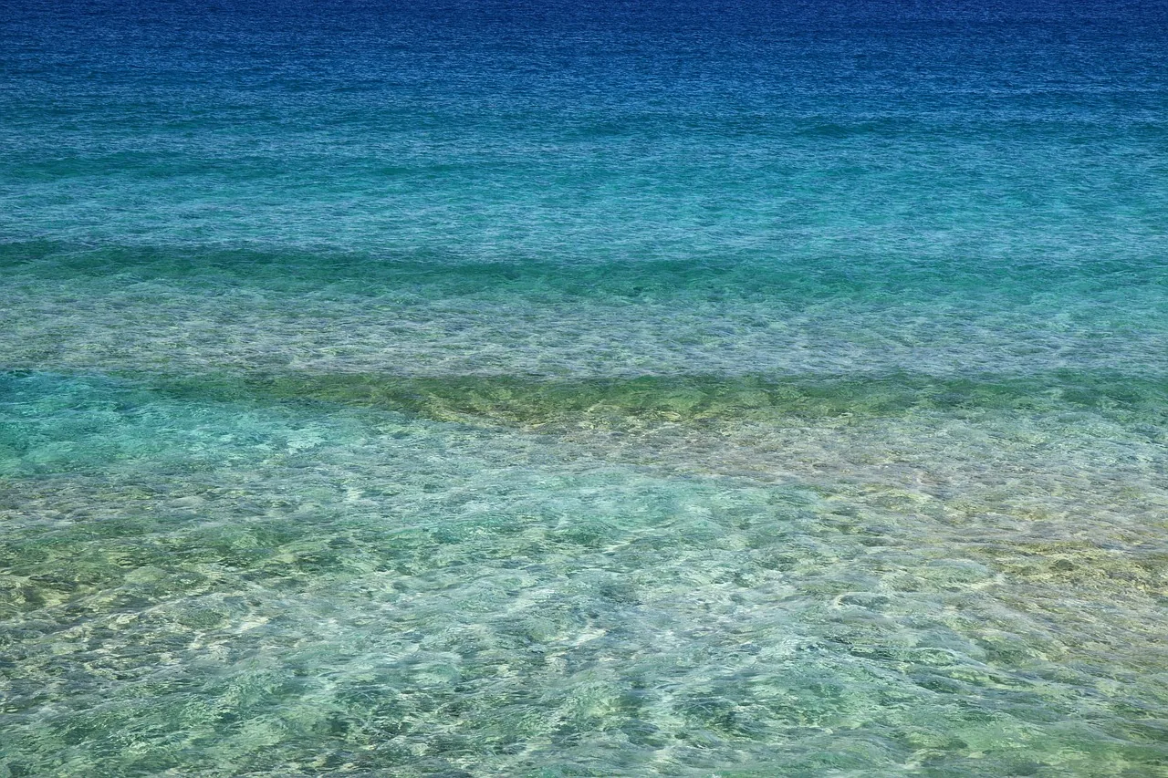 Clear shallow seawater transitioning from turquoise to deep blue with sandy bottom visible
