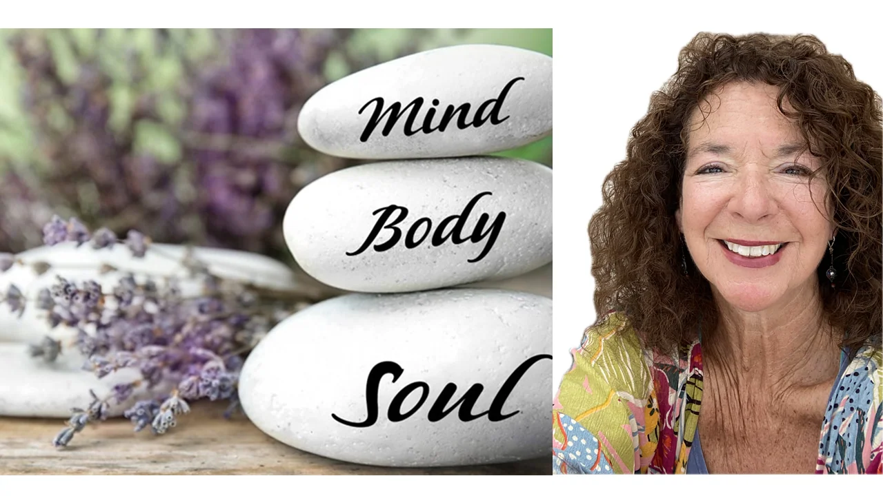 Woman with curly brown hair smiling next to stacked white stones labeled Mind Body Soul with lavender flowers